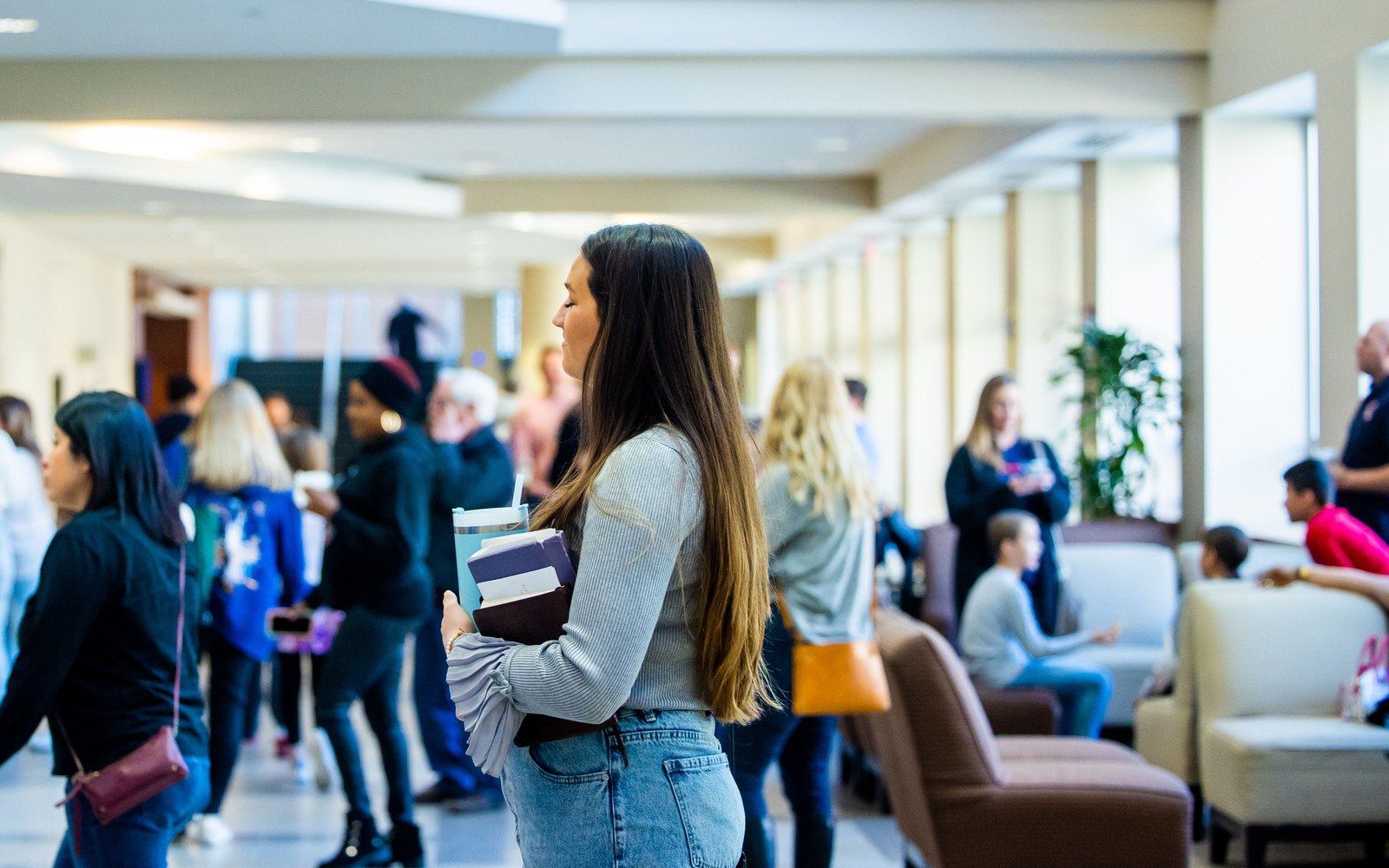 Une étudiante avec des livres dans un couloir de campus animé.