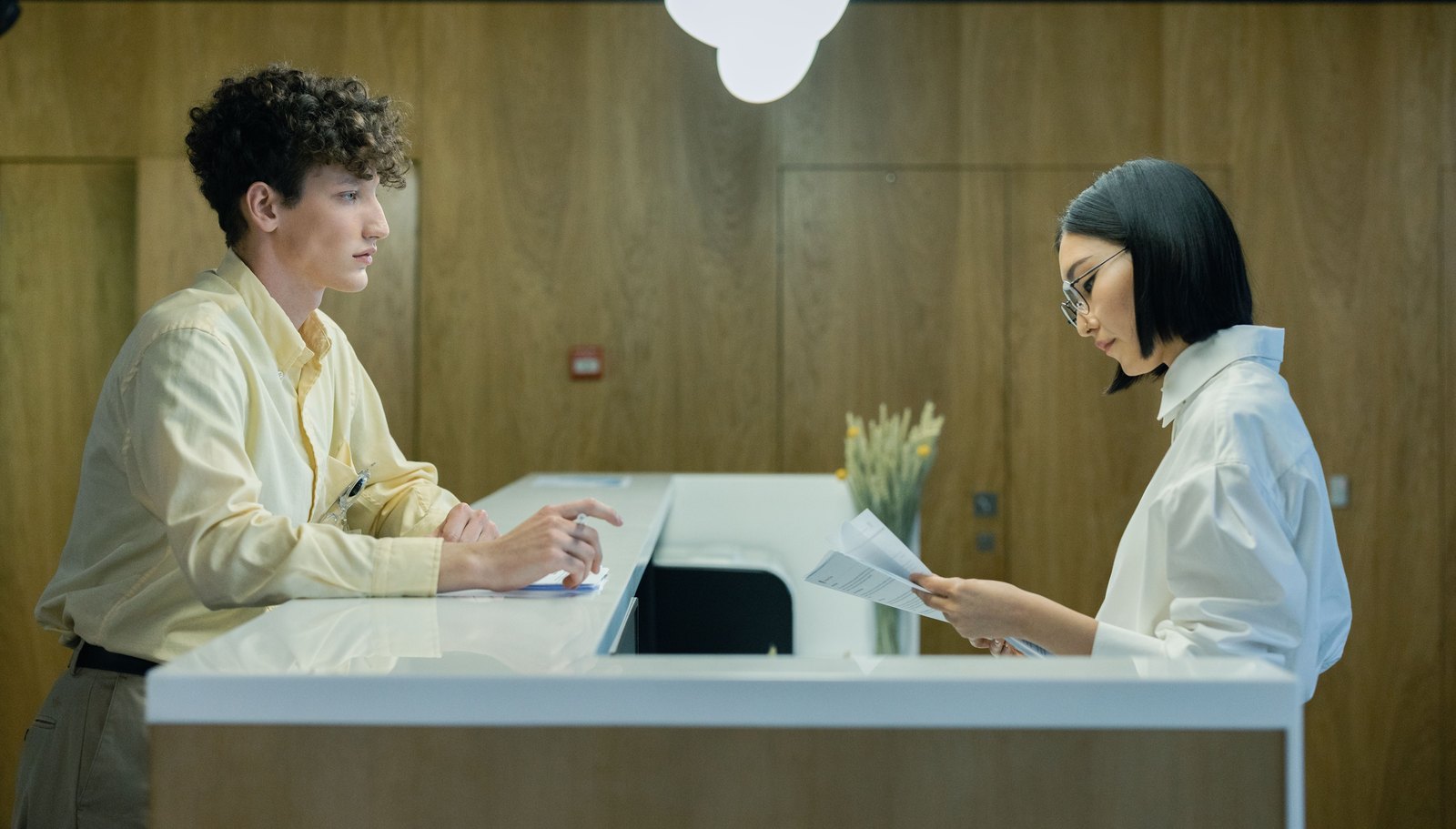 Un visiteur et une employée consultent des documents à un comptoir d’accueil.